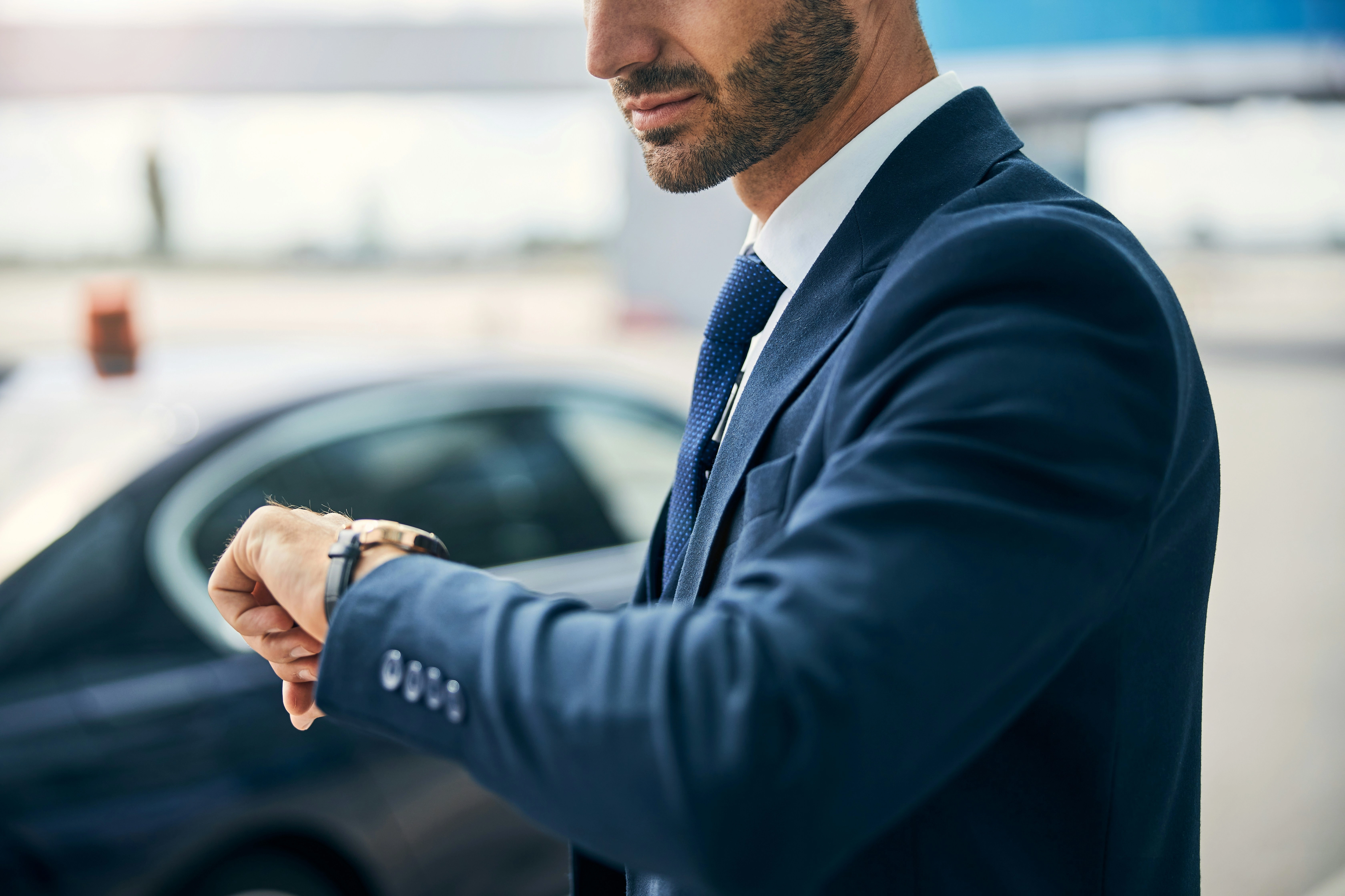 Professional chauffeur checking time with luxury vehicle at airport